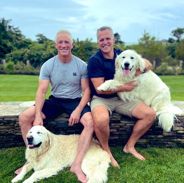 Image of Stephen and Rufus and their dogs sitting on a stone wall in their back yard.